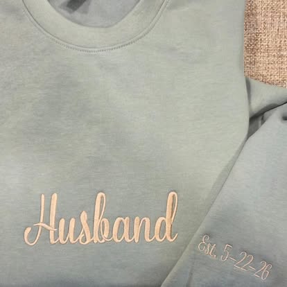 Sage-green crewneck with 'Husband' embroidered in script and a date stitched on the cuff
