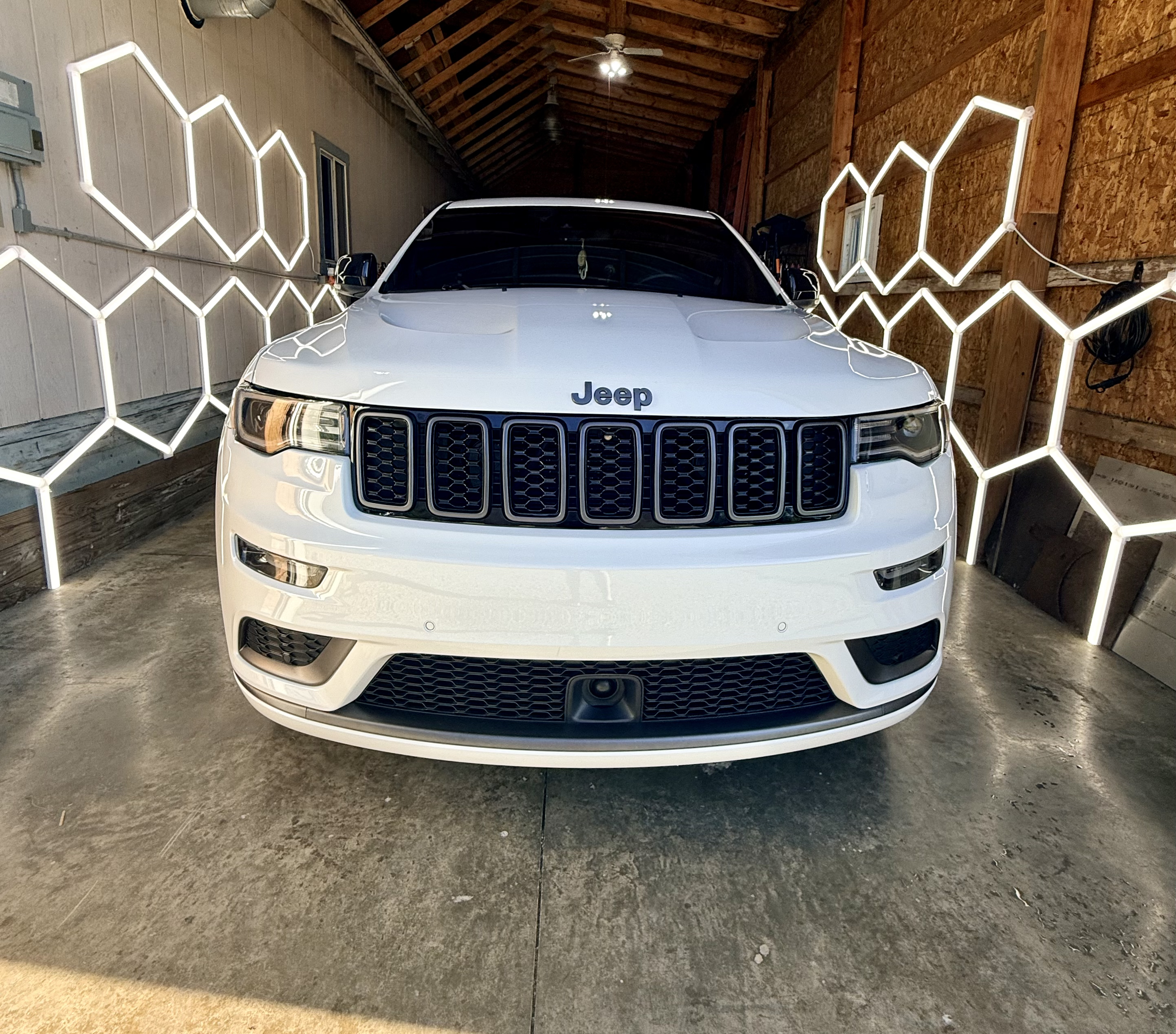 A freshly detailed white Jeep Grand Cherokee glowing under hexagon LED lights in the barn