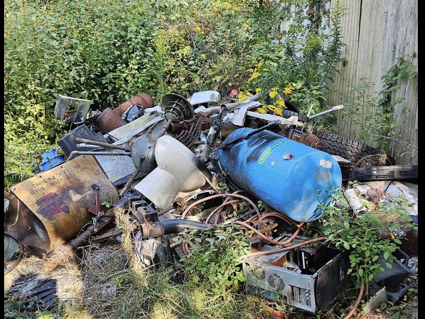 A corner of a yard buried under scrap metal, tyres, a water tank and old computer cases
