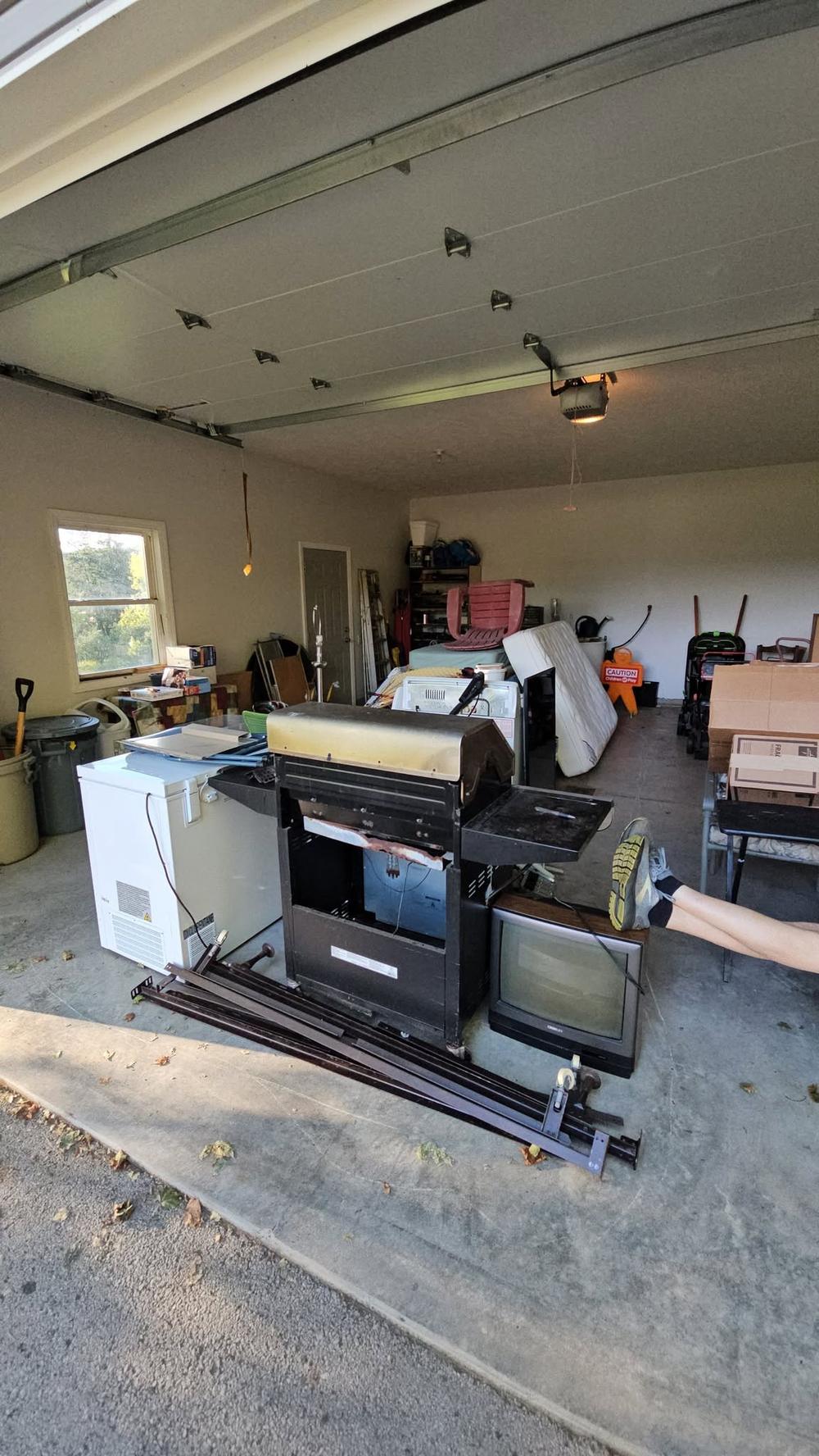 A load staged in a garage doorway: chest freezer, grill, tube television, mattress and bed rails