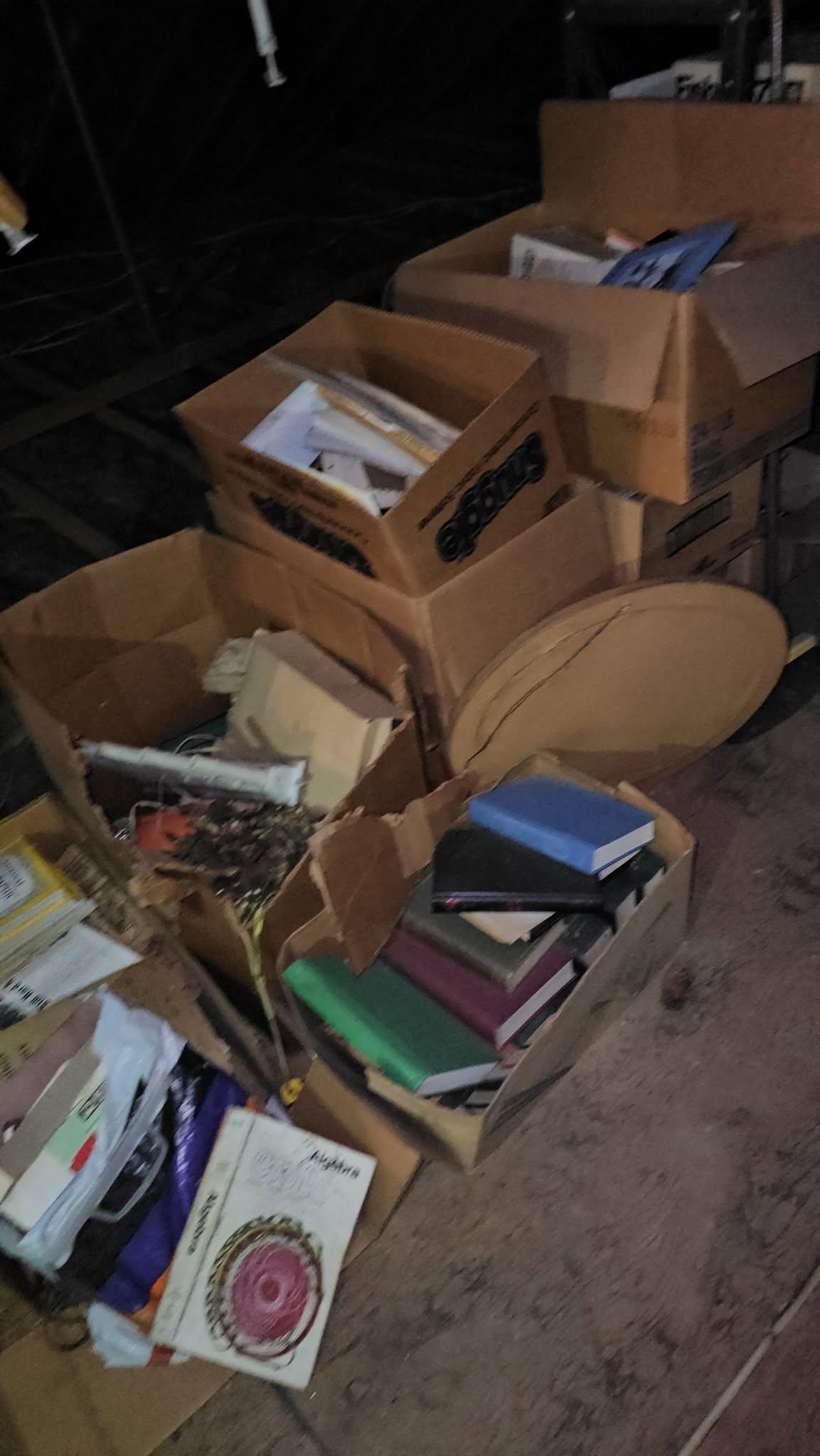 A dark basement floor covered in collapsing cardboard boxes of damp paperwork, books and debris