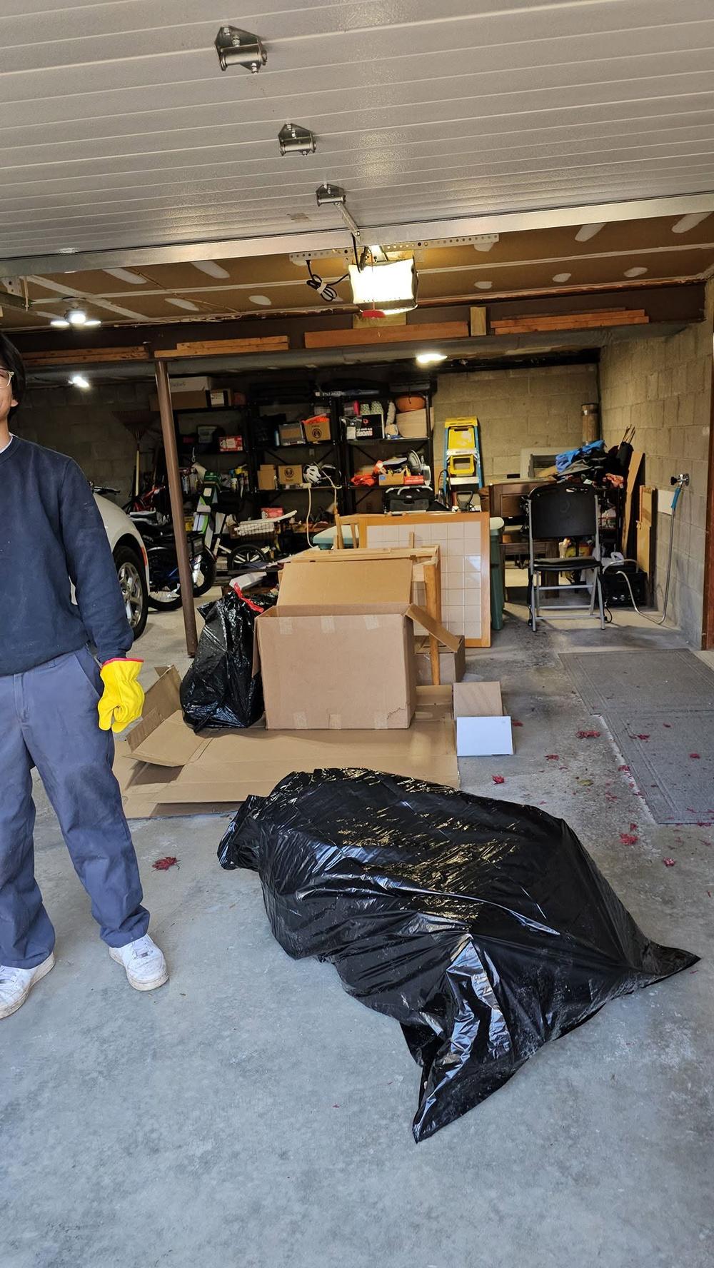 A cleanout underway: gloved hands, cardboard boxes and contractor bags stacked in a garage doorway