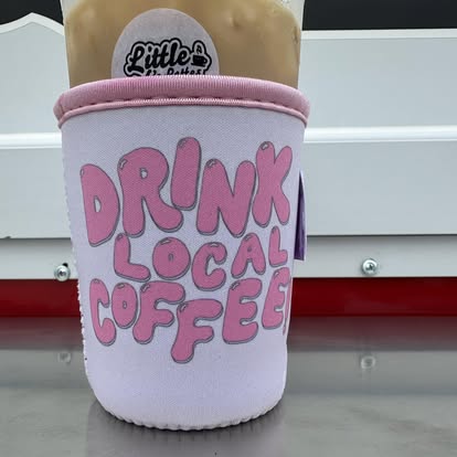 A pink DRINK LOCAL COFFEE koozie wrapped around an iced drink