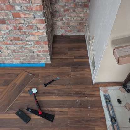 Scott installing luxury vinyl plank flooring next to an exposed brick wall